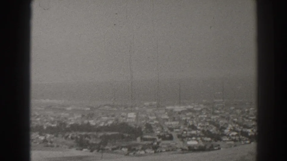 Long Beach residential blocks appear below a hazy coastal horizon in this scratched black-and-white 8mm frame from 1937.