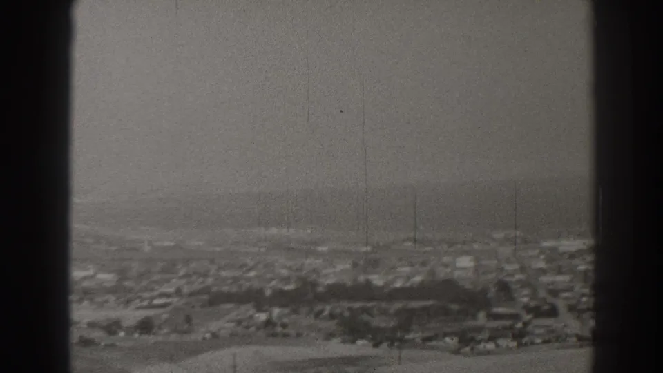 1937 Long Beach home-movie frame showing a distant residential grid, low buildings, trees, and soft haze through black 8mm borders.