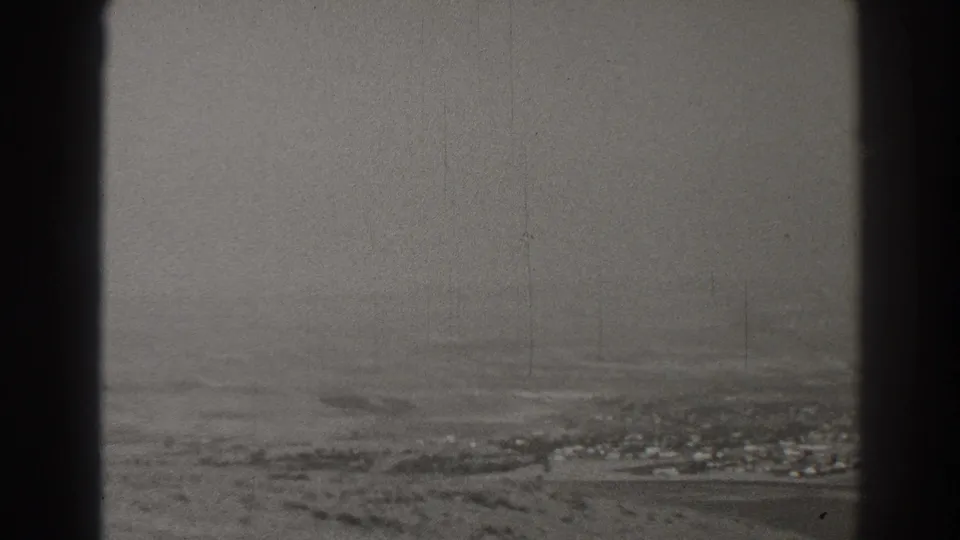 Hazy 1937 Long Beach aerial view with open ground, distant settlement, and a dark window edge at right.
