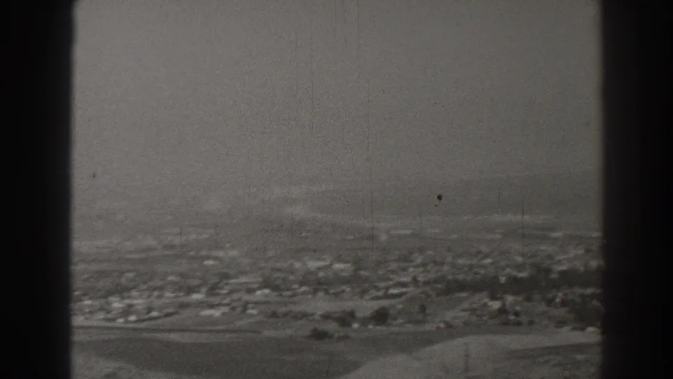 Black-and-white 1937 Long Beach aerial view with low buildings, roads, open land, and dark aircraft window bars in the foreground.
