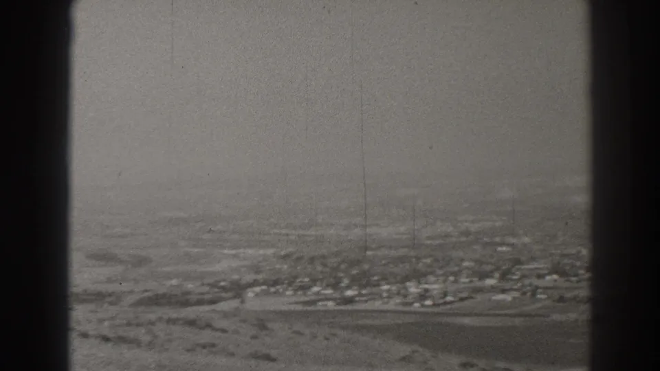 Grainy 1937 aerial home-movie frame showing a Long Beach-area settlement, roads, and open land through aircraft window framing.