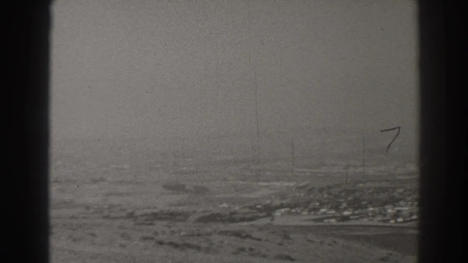 Black-and-white Long Beach aerial view with town blocks, open terrain, haze, and visible film wear near the end of the clip.