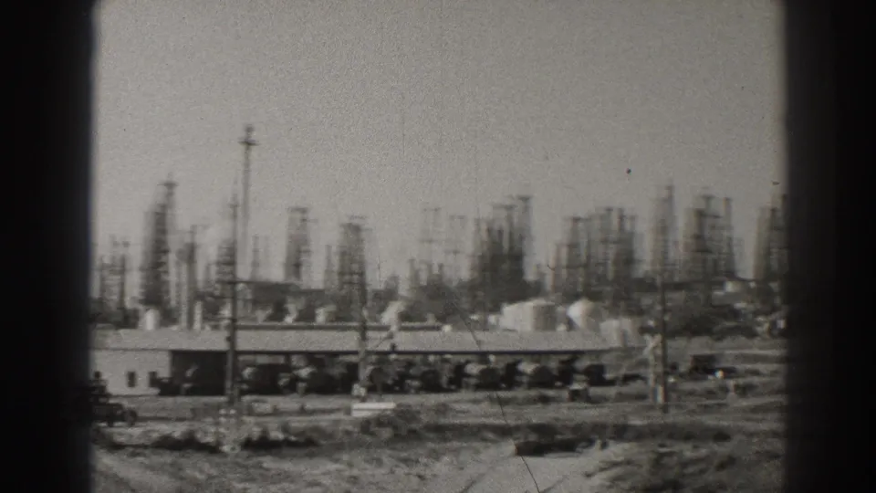 Soft-focus 1937 Signal Hill oil-field frame showing clustered derricks, low buildings, utility poles, and rough open ground.
