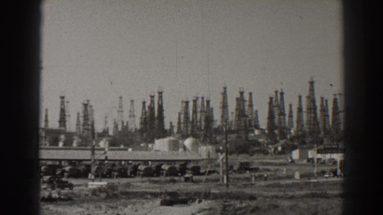 1937 Long Beach oilfield view with dense derricks beyond a roadside foreground, low buildings, tanks, and utility poles.