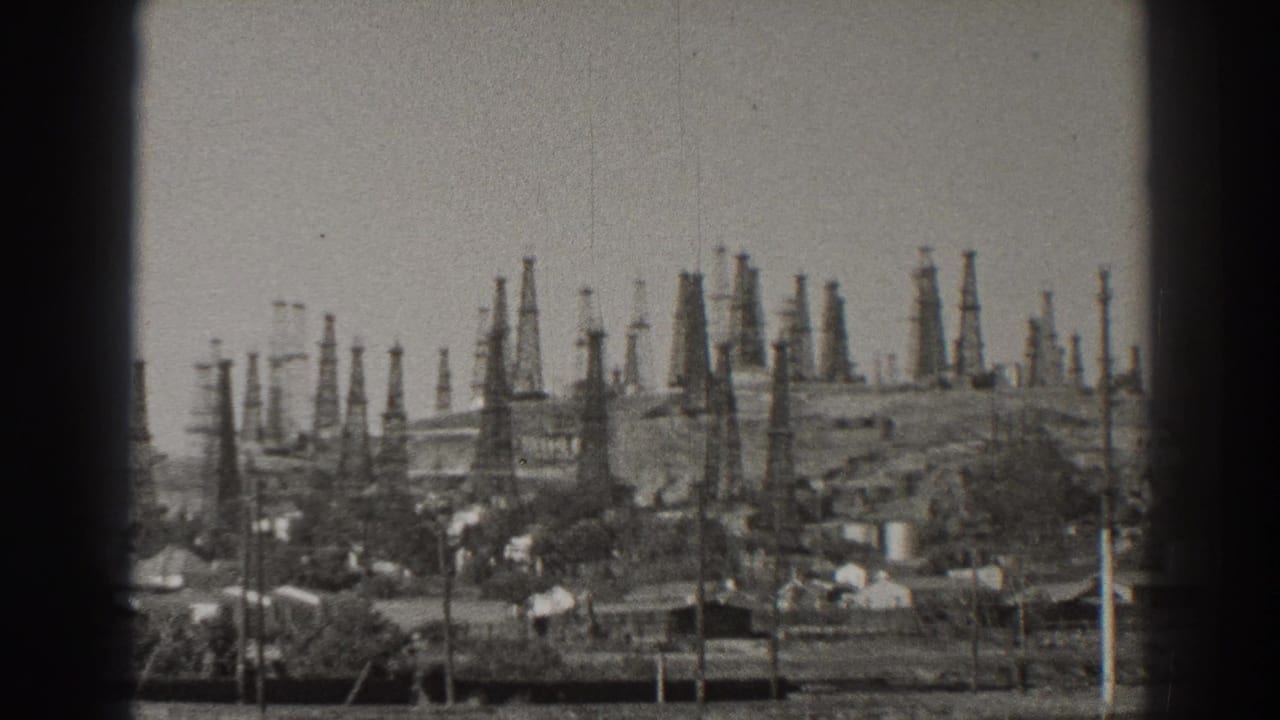 1937 Long Beach home-movie frame showing many oil derricks rising over a small neighborhood and utility poles.