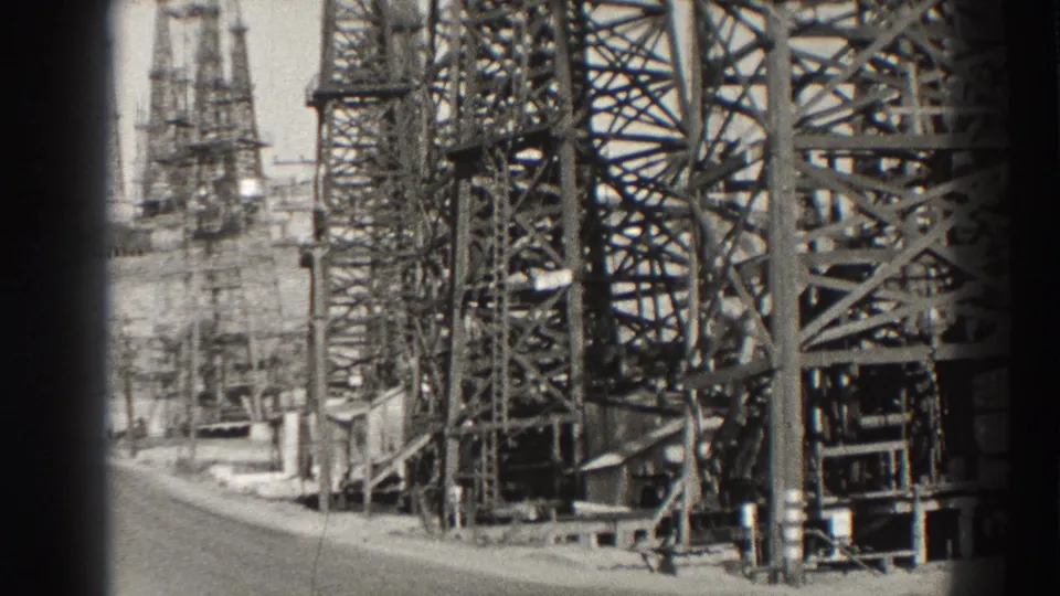 1937 Long Beach 8mm frame showing clustered steel oil derricks and support structures under a bright sky.