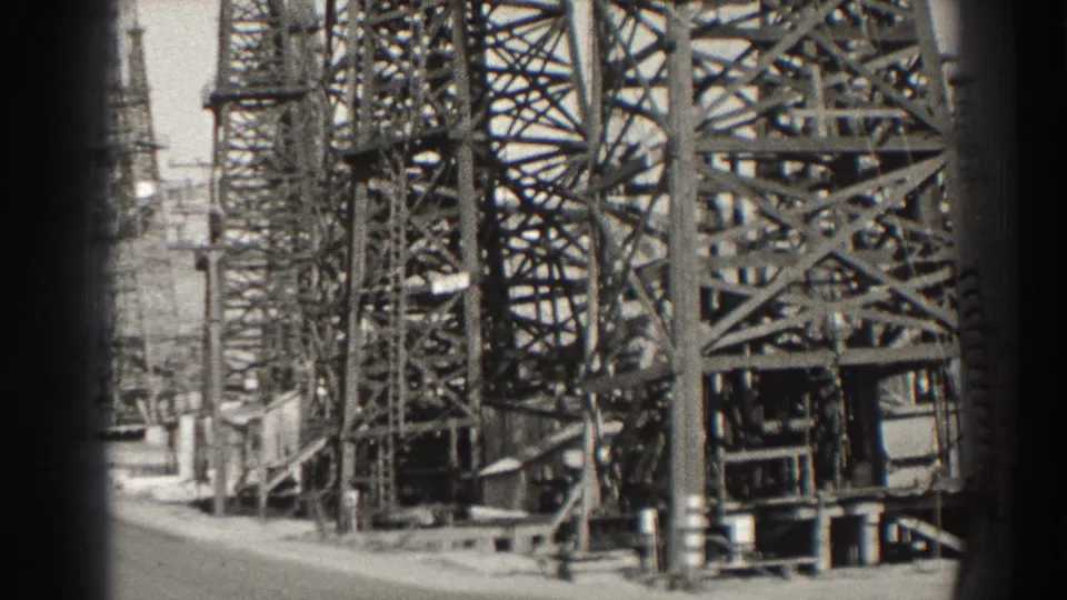 Black-and-white 1937 Long Beach frame with dense oil derrick latticework, pump equipment, and vertical film borders.