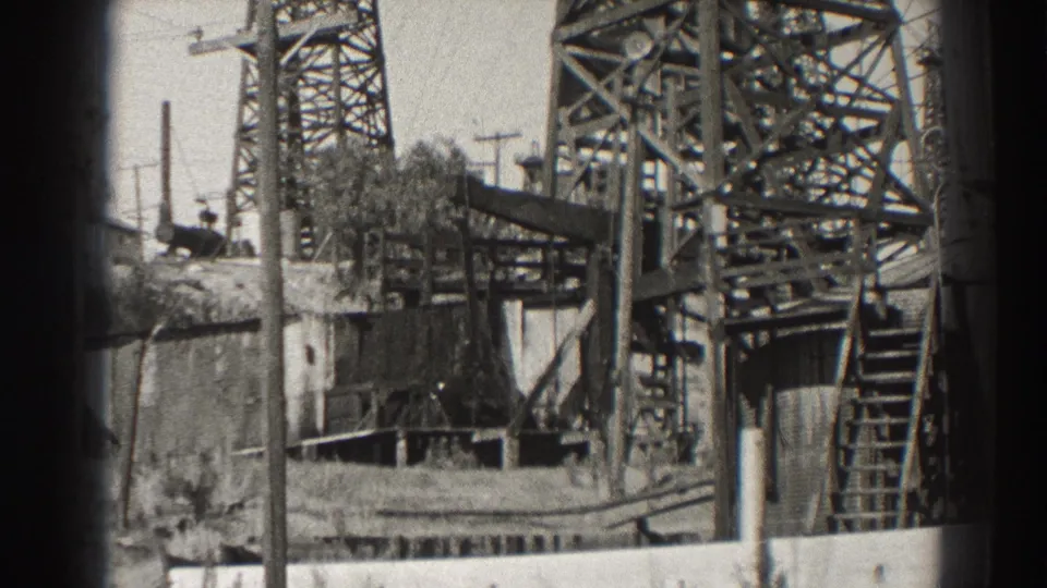 1937 Long Beach oil well frame showing the lower derrick, ladder, platform, base structure, utility pole, and sparse brush.