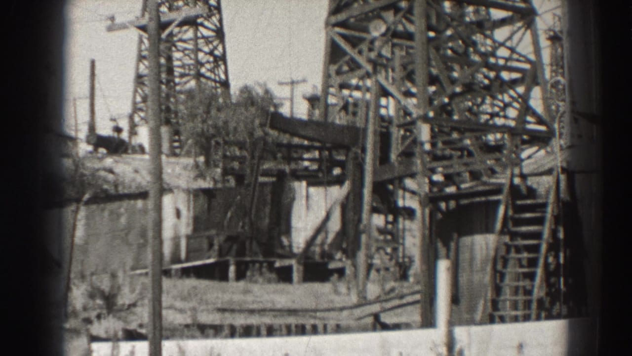 Close view of steel oil derrick supports, ladder, wall, and utility poles.