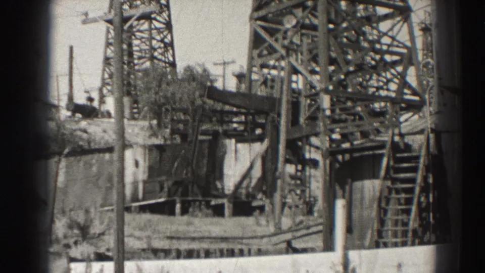 Steel oil derrick supports and a ladder stand above a walled industrial area in the 1937 Long Beach footage.