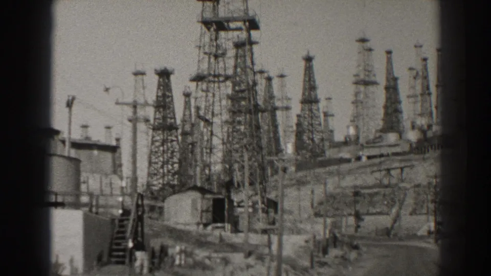 1937 Long Beach 8mm frame with multiple transmission towers, utility poles, tanks, and service structures under a bright sky.