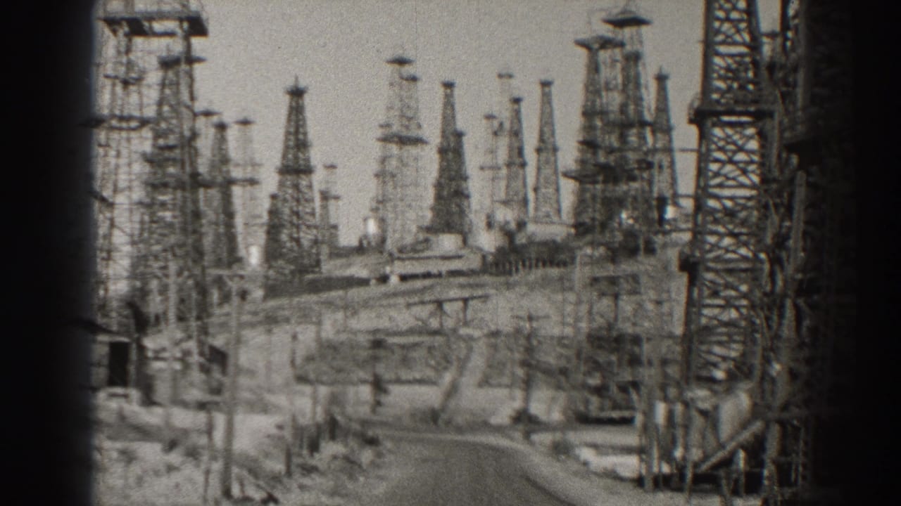 1937 Long Beach oil-field view with many steel derricks rising beyond a winding service road.