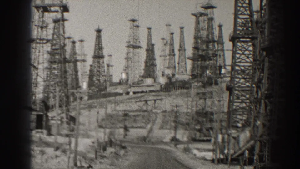 1937 Long Beach oil-field view with many steel derricks rising beyond a winding service road.