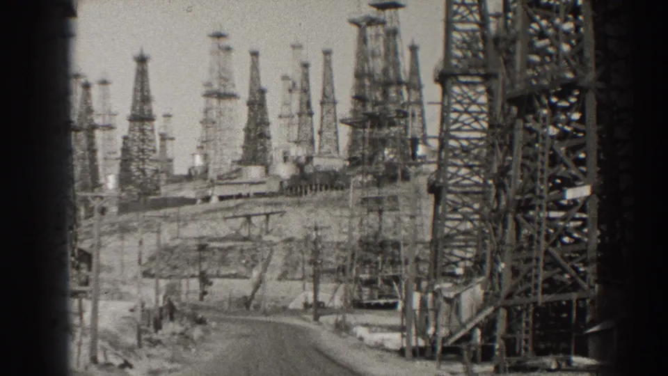 Black-and-white 8mm view of a Long Beach oil field with derrick towers clustered around a curving road.