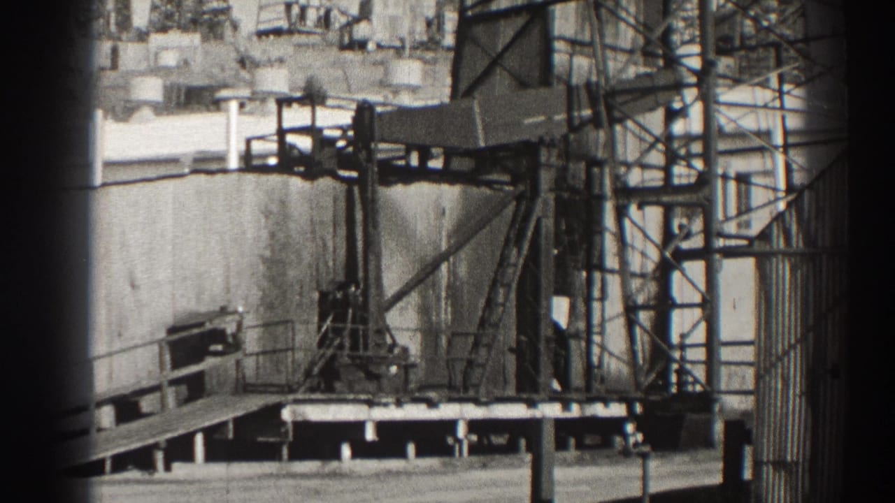 Oil pumpjack beside metal scaffolding and industrial tanks.