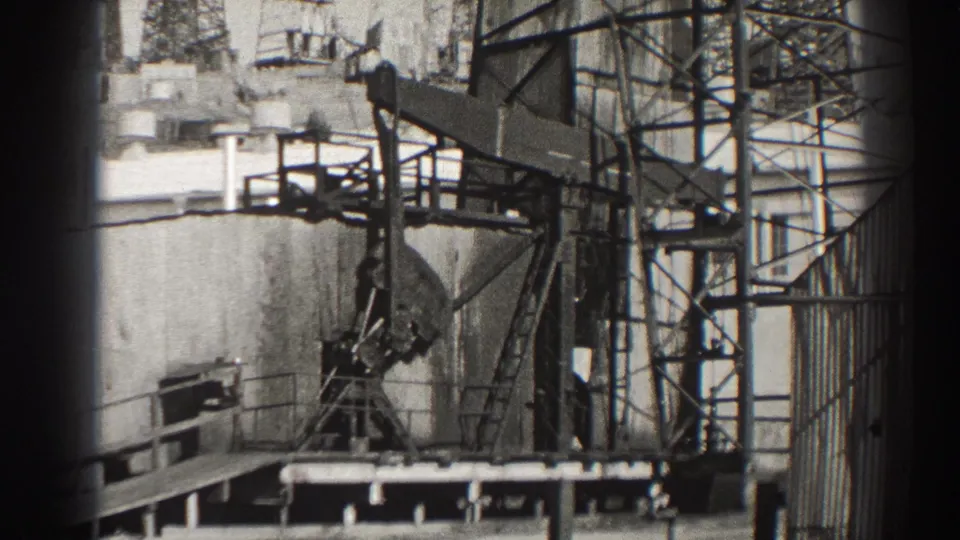 Black-and-white 8mm frame of a Long Beach oil pumpjack with its counterweight low near a platform and lattice supports behind it.