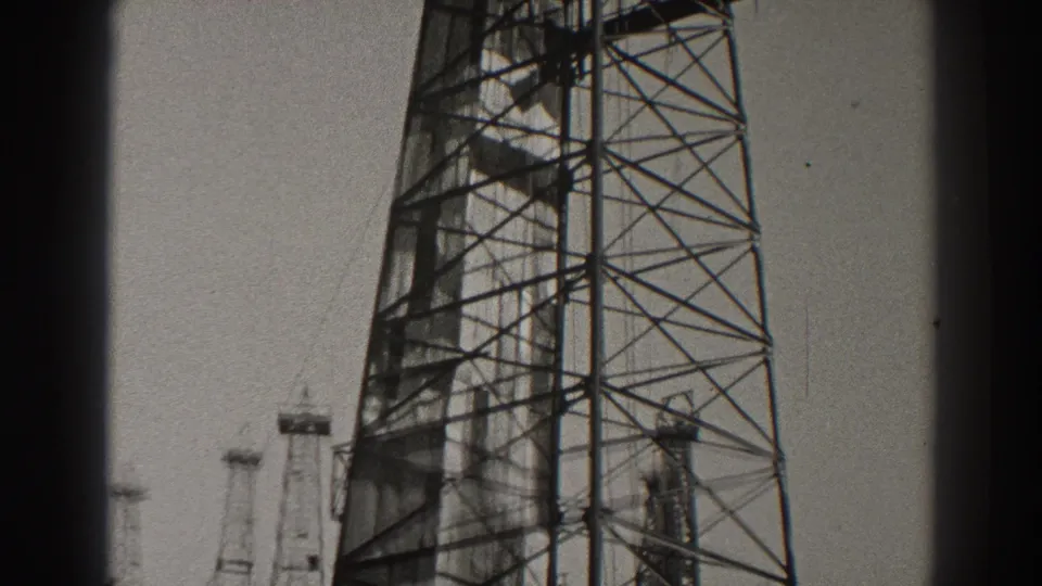 1937 Long Beach 8mm still showing the middle section of a tall oil derrick, its cross-bracing, and smaller towers low in the background.