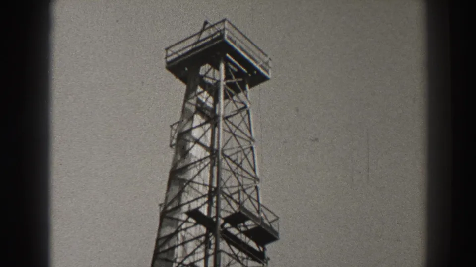 1937 Long Beach home-movie frame showing a taller section of the metal lattice tower from below, with platforms at different levels.