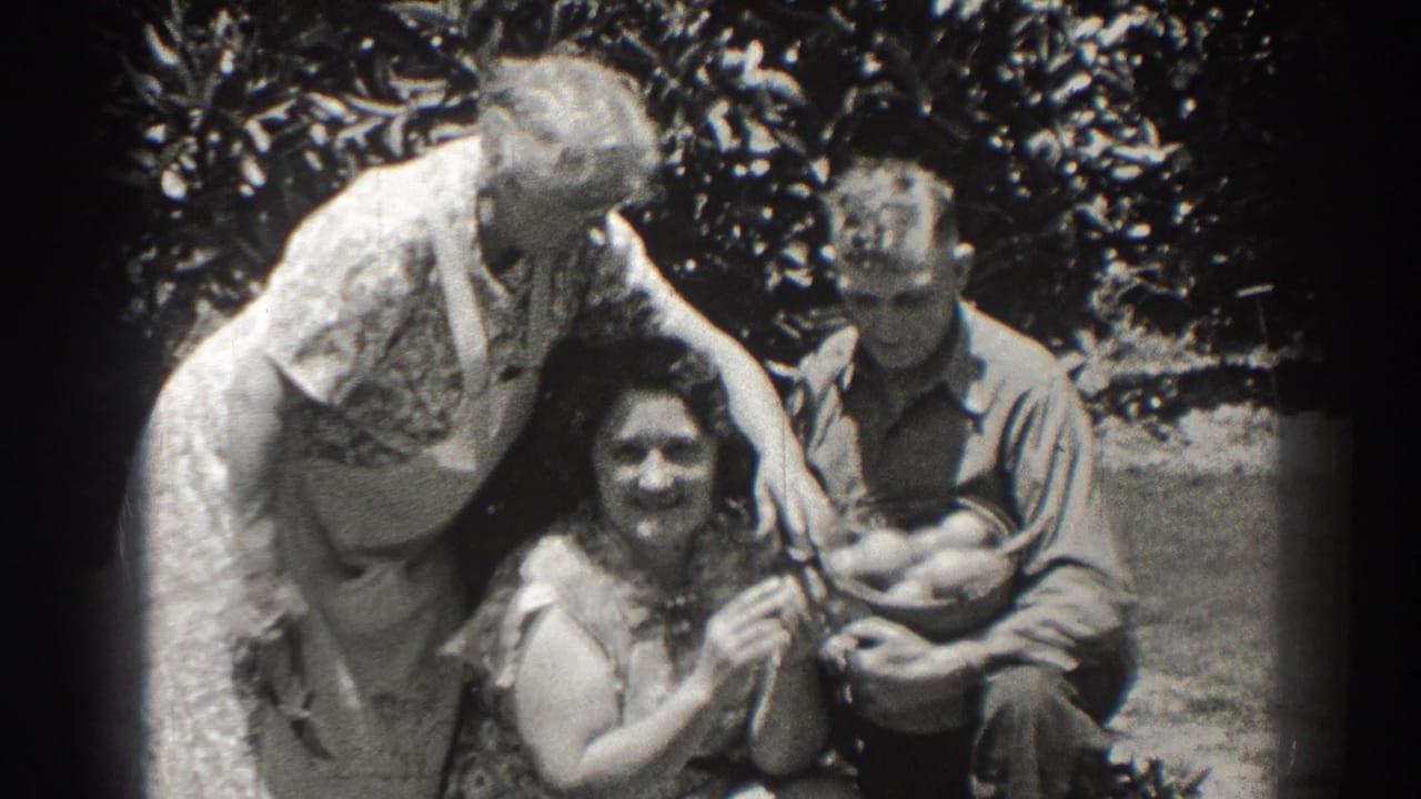 Three adults outdoors as a woman in an apron reaches toward a basket held by a seated man.