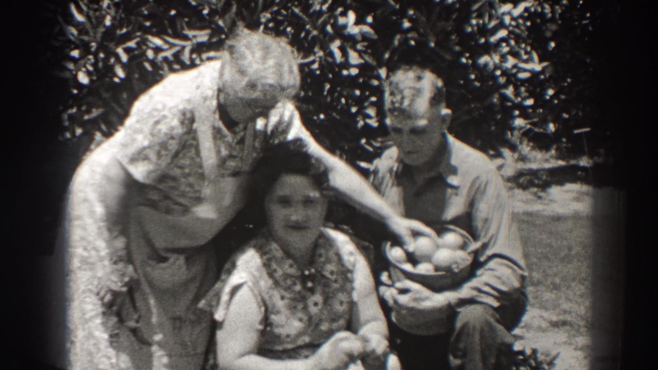 1937 Long Beach home-movie frame of three adults outdoors, with a woman leaning over another woman while a man holds a basket of fruit.