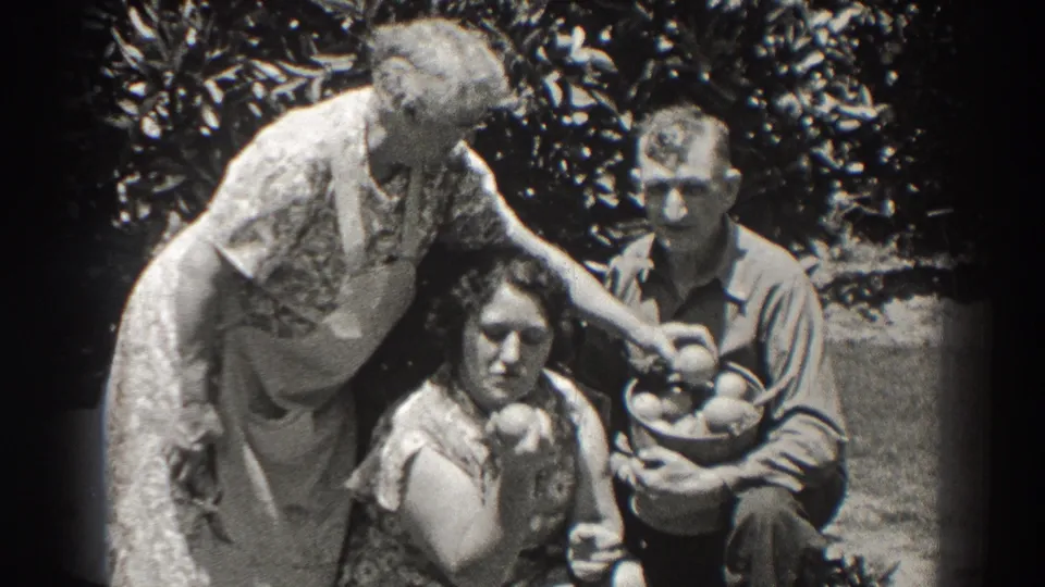 Final frame of the 1937 Long Beach family garden clip, with three adults gathered around fruit under leafy trees.