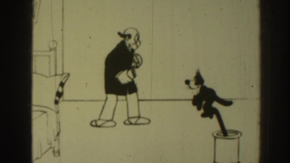 1937 8mm cartoon frame with a dark-suited animated man in a simple room and a small cat figure moving from a stand.