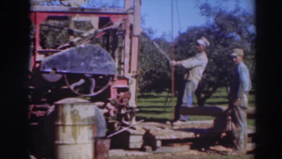 1937 Sacramento orchard footage showing two men around a portable sawmill, with barrels and timber supports visible nearby.