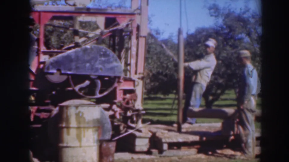 In a 1937 Sacramento orchard scene, one man works the drilling rig while another watches beside the machinery.
