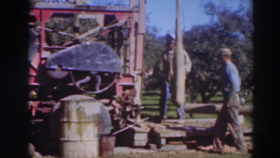 A Sacramento orchard work scene shows one man near the red rig and another moving a long pipe or pole at the edge of the frame.