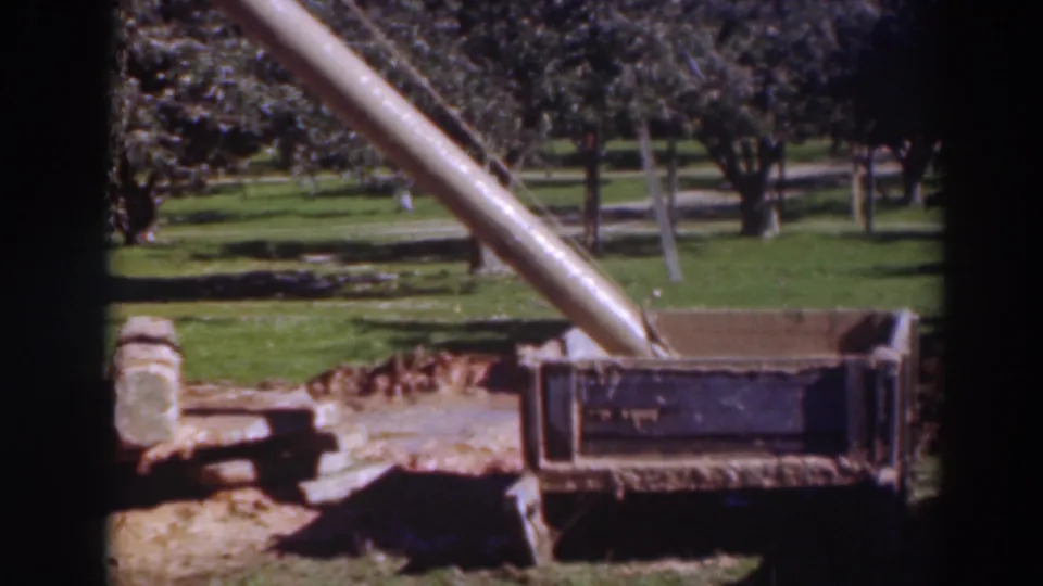 A closer 8mm view of the wooden chute and crate in the 1937 Sacramento orchard, with tree trunks and grass in the background.