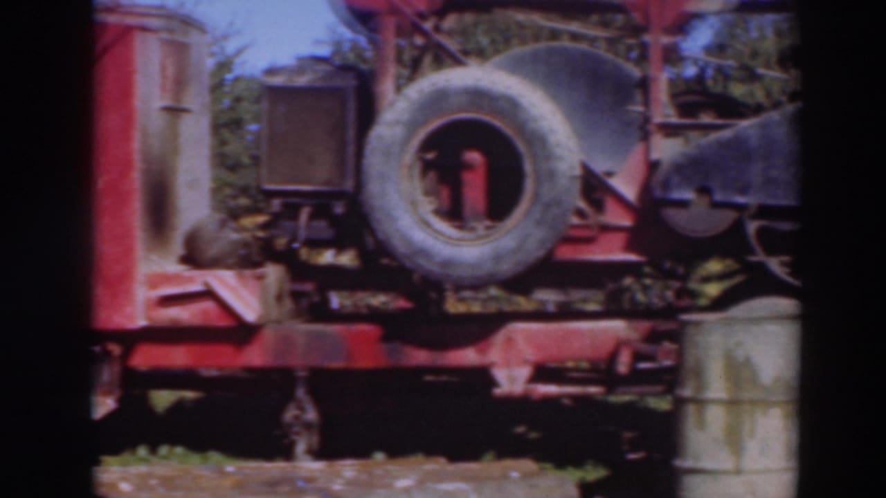 Red industrial machine with spare tire and metal parts in an outdoor grassy area.