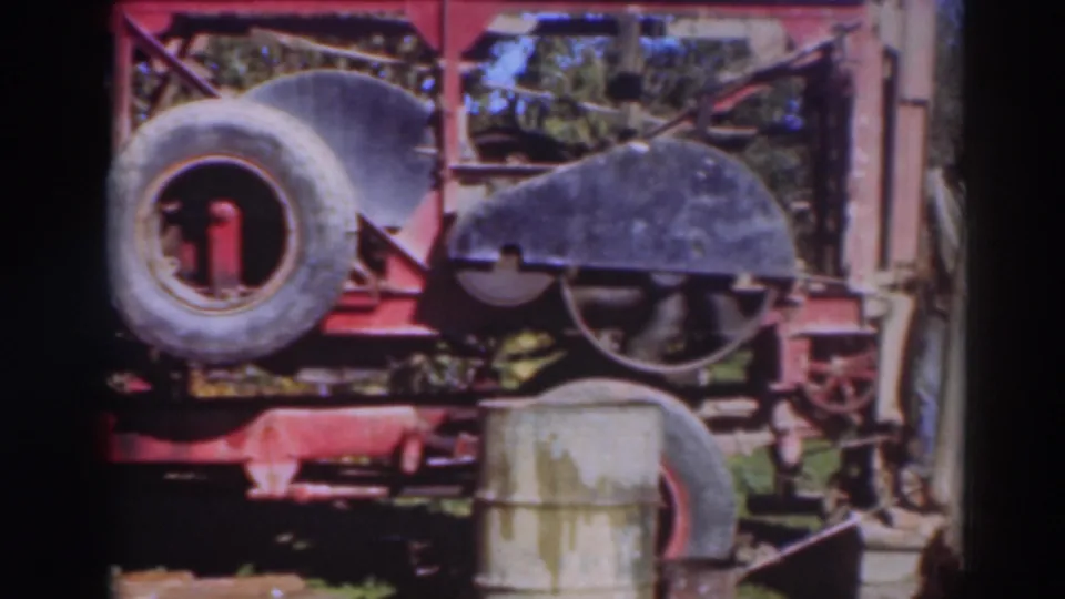 1937 Sacramento frame with a red machine, spare tire, curved guard, metal drum, and trees visible behind the equipment.