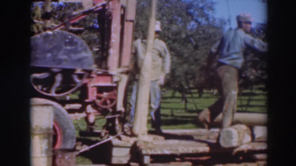 1937 Sacramento frame showing two adult men beside red industrial equipment in a grassy, tree-lined outdoor area.