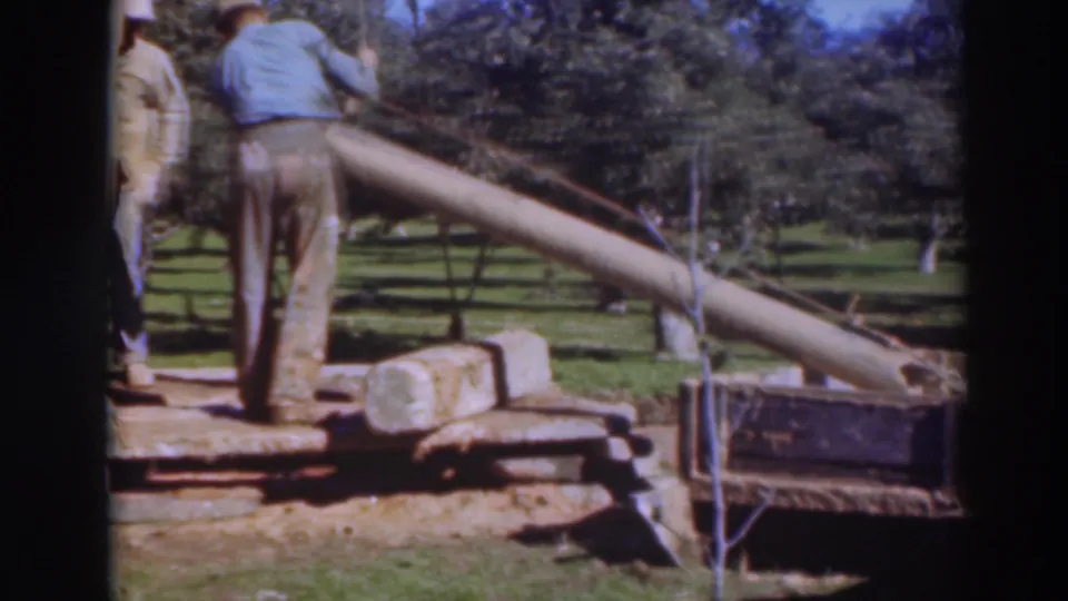 1937 Sacramento-area outdoor work frame showing a long beam being moved near saw equipment, with trees and grass behind.
