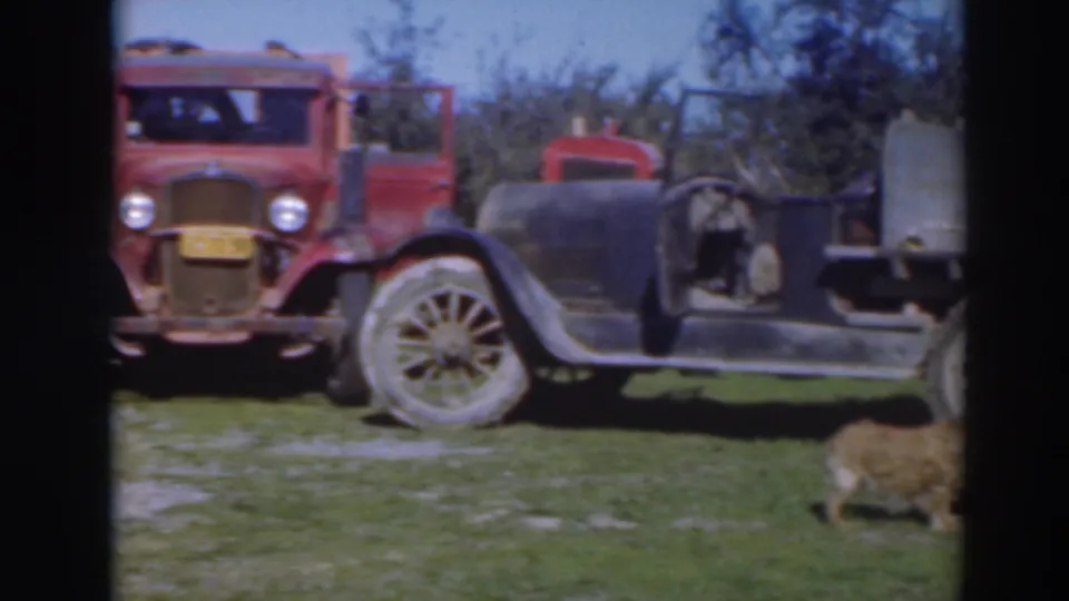 Parked 1930s-era vehicles are shown in the Sacramento orchard footage, including a red vehicle and an older car body.