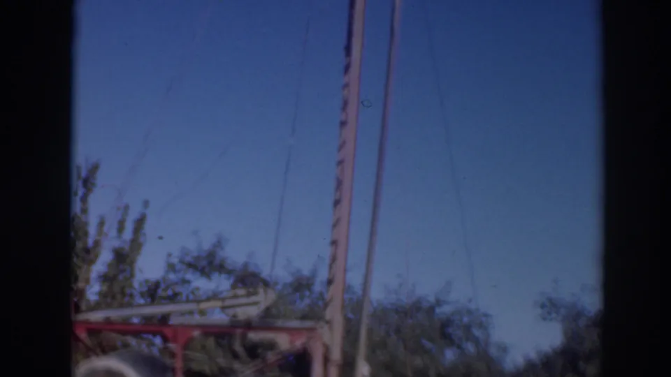 1937 Sacramento-area frame with red equipment partly visible below tall poles and cables against trees and sky.