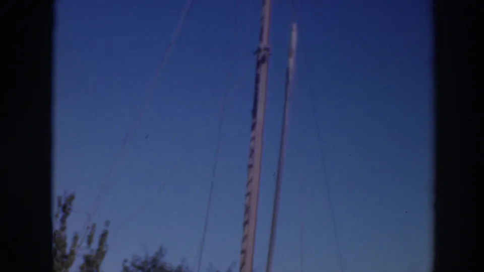 8mm frame from the Sacramento-area clip showing poles and rigging lines rising above trees into open sky.