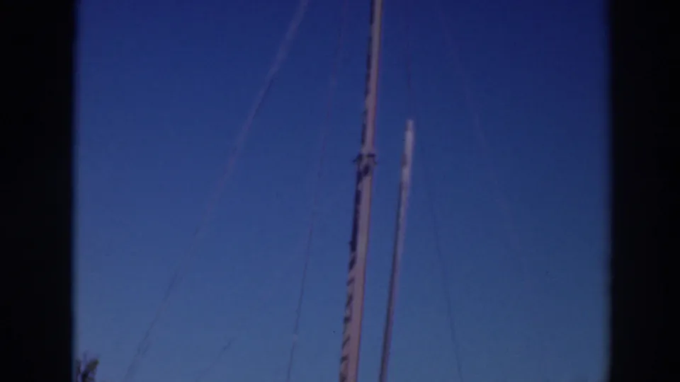 Final 1937 Sacramento-area frame focusing on tall poles, cables, blue sky, and treetops at the edge of the worksite.
