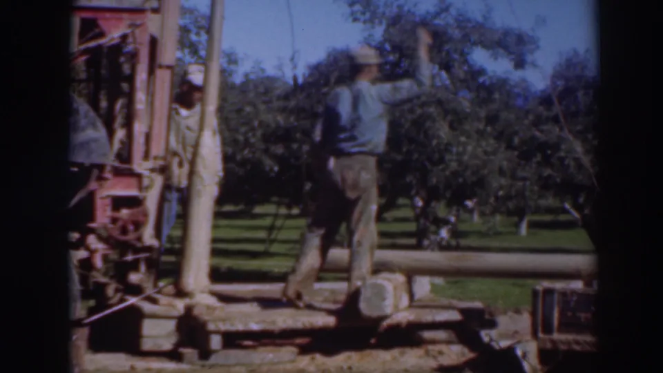 In 1937 Sacramento orchard footage, a man stands near a large mechanical apparatus while another worker is partly visible nearby.