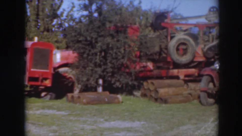 Home-movie frame from Sacramento in 1937 showing cropped red machinery, a salvage vehicle, logs, and trees.