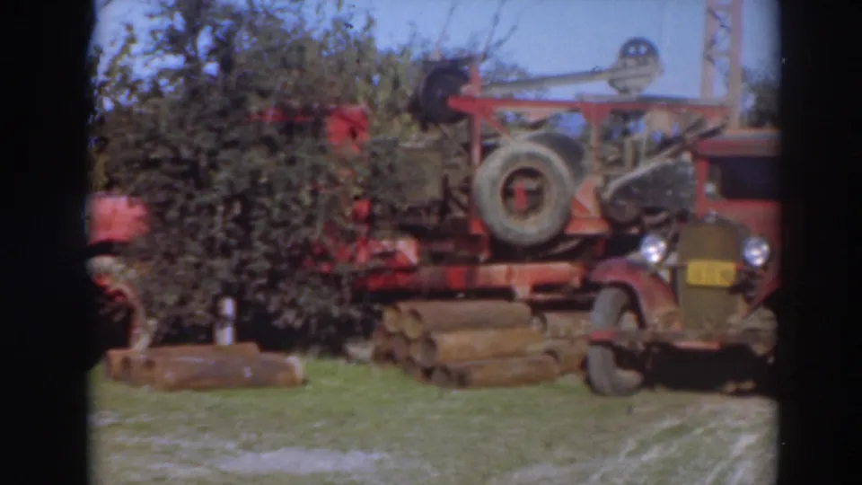 1937 Sacramento frame showing red industrial salvage equipment, a truck front, logs, trees, and grass.