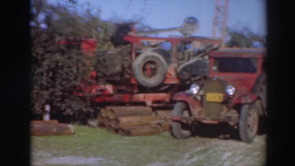 1937 Sacramento home-movie frame showing a red work truck near logging equipment, timber stacks, trees, and blue sky.