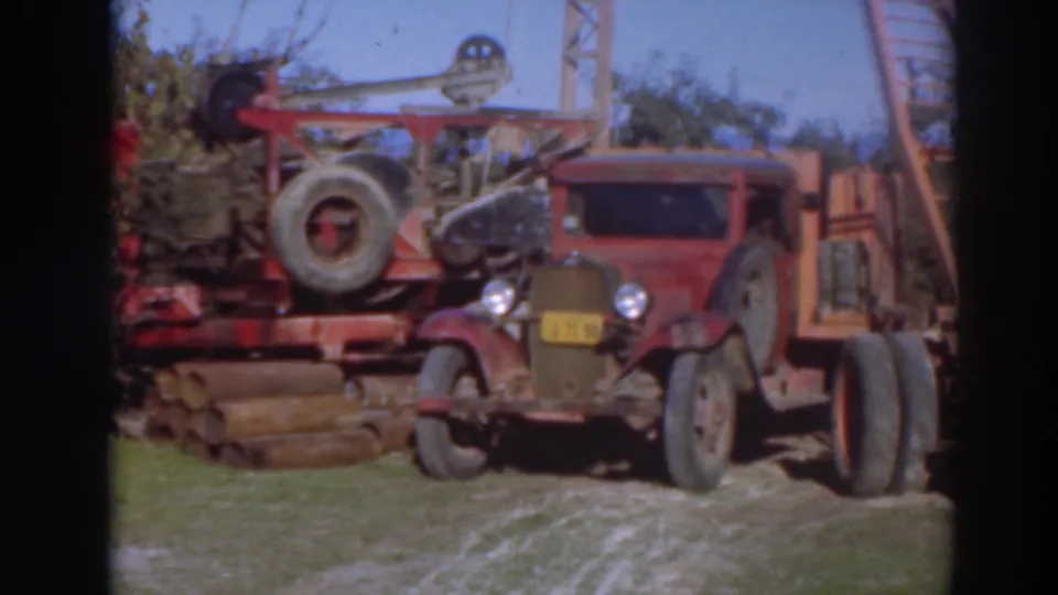 Red vintage truck and crane equipment are framed more clearly at a Sacramento logging site, with logs and trees behind them.
