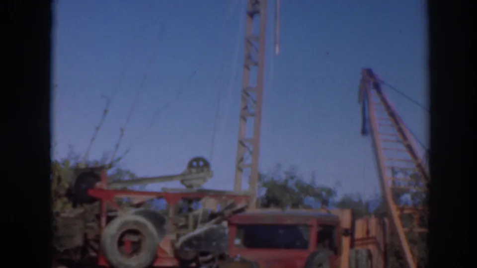The final frame shifts toward the crane boom and truck roof, keeping the logging yard, timber, and blue sky in view.