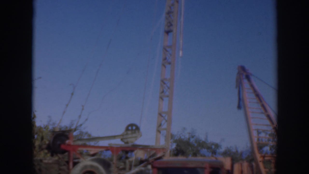 1937 Sacramento home-movie frame showing a red crane boom, pulley wheel, cables, and vertical mast under a clear blue sky.