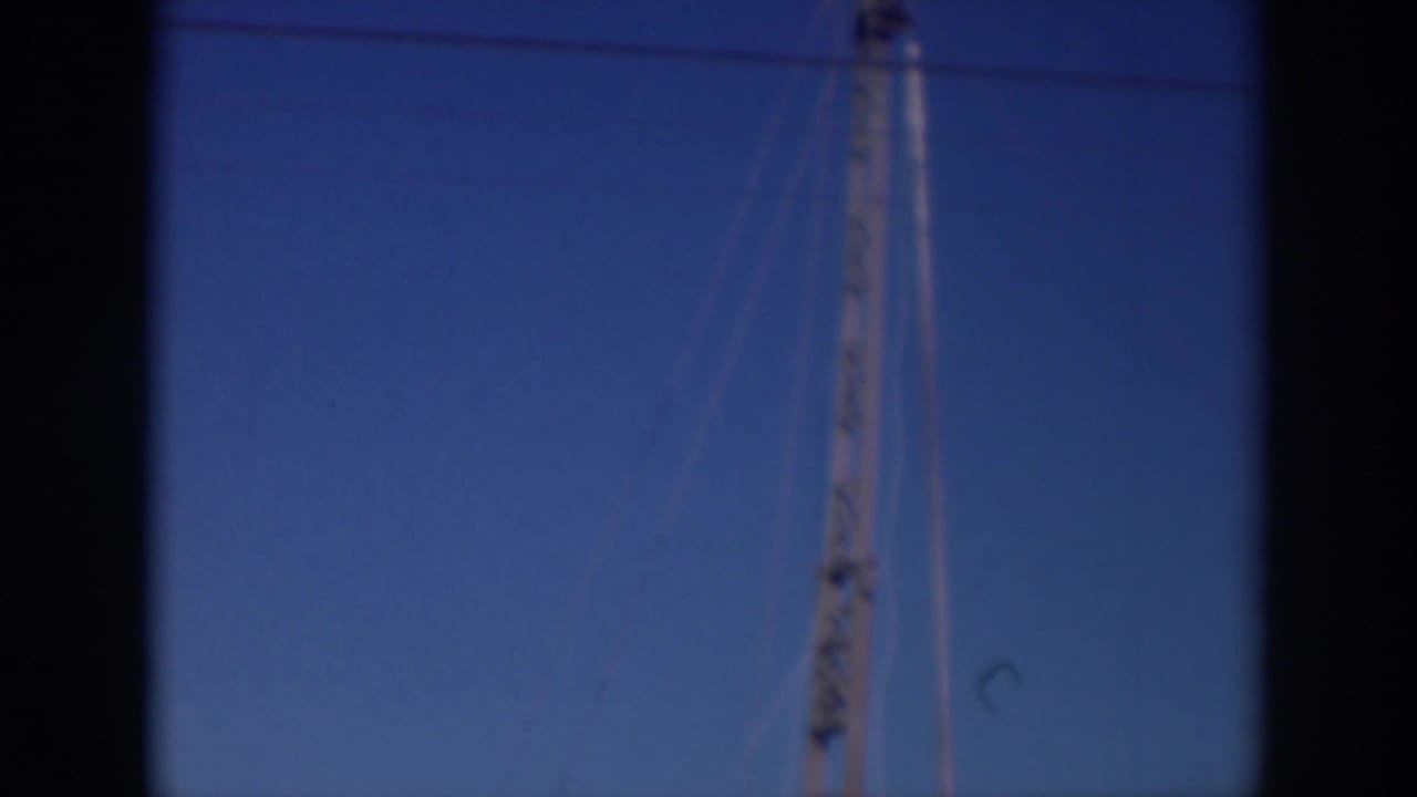 Tall pole-like structure and wire against a blue sky with dark film borders.