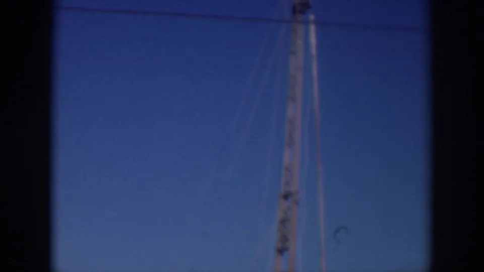 1937 Sacramento home-movie frame showing a tall brown pole or rig section rising into a clear blue sky with visible film-edge shadowing.