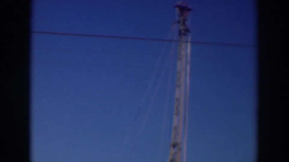 1937 Sacramento frame with a tall brown lattice-like structure, overhead wire, and dark vertical film border against blue sky.