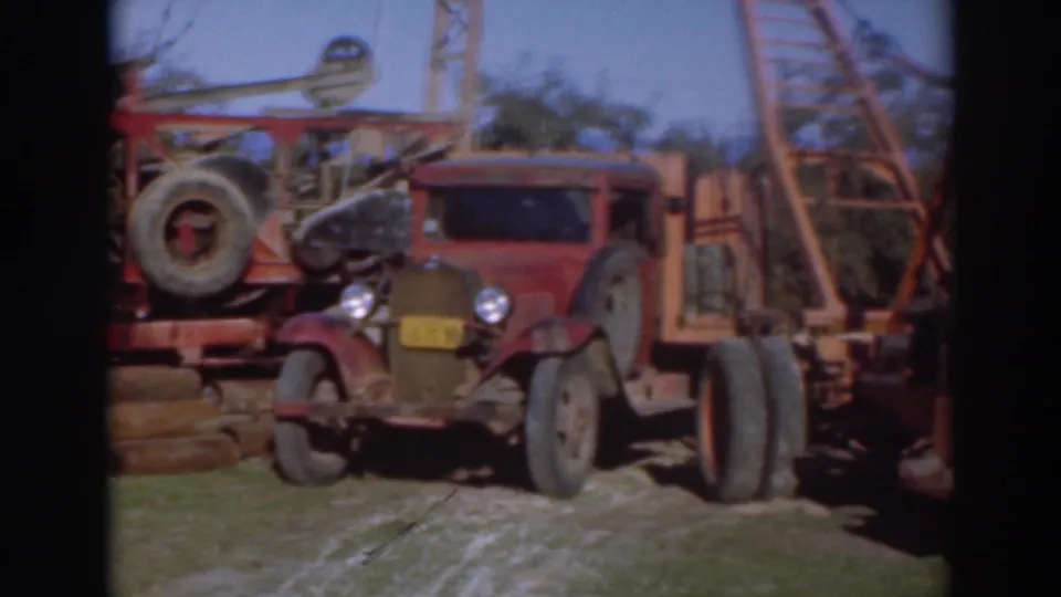 1937 Sacramento home-movie frame showing an older red truck, wheels, lattice equipment, grass, trees, and a dark film border.