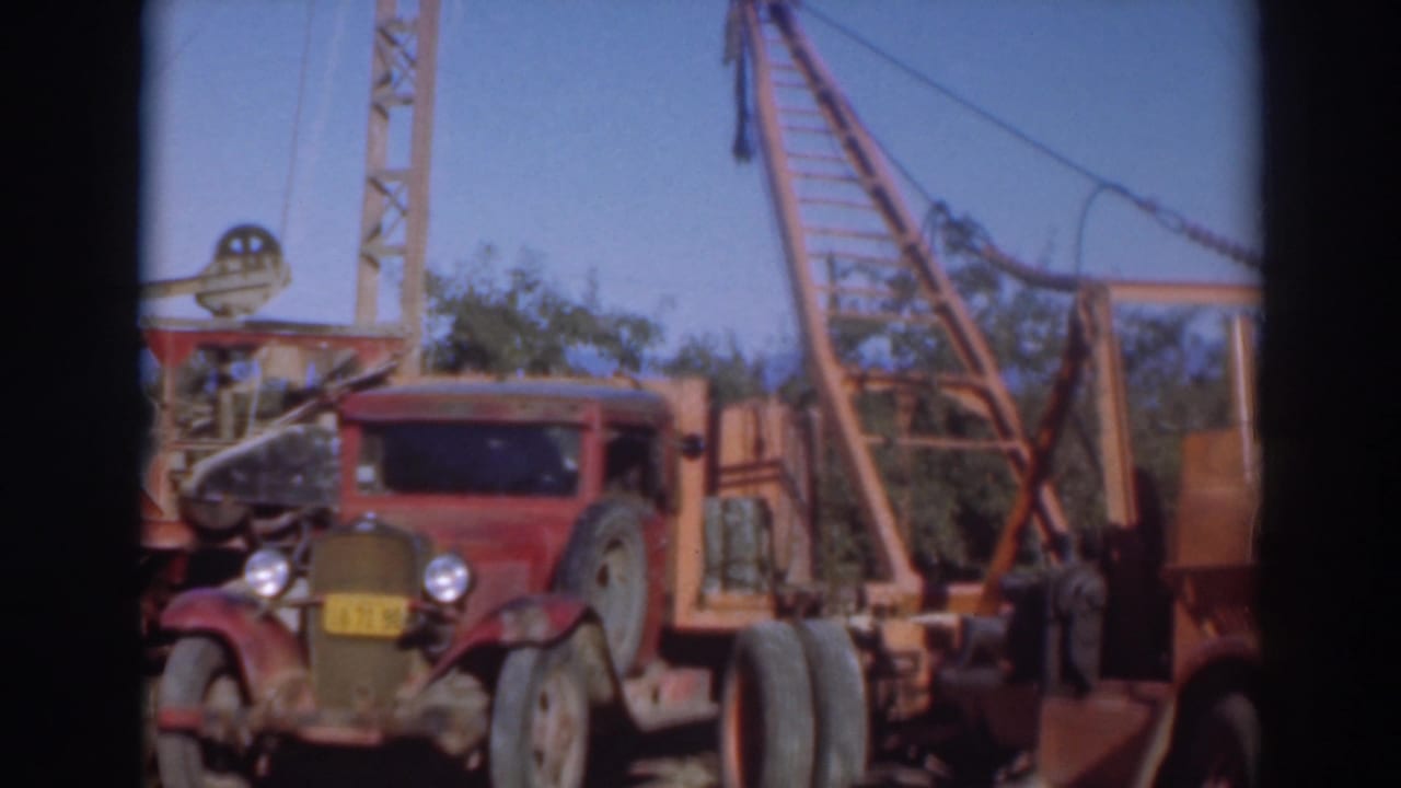 Red vintage truck beside a tall crane structure in an outdoor yard.